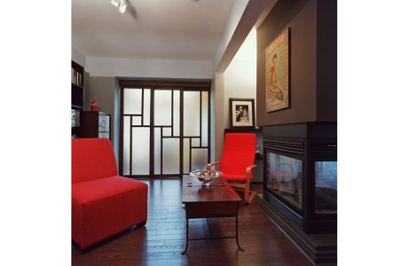2 red chairs form sitting area in front of 4 sided fireplace, sliding opaque doors closed blocking view to separate room beyond,