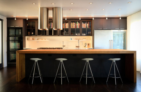 Kitchen with dark gray cabinets, a large oak island and two stainless steel tubes over the cook top, modern