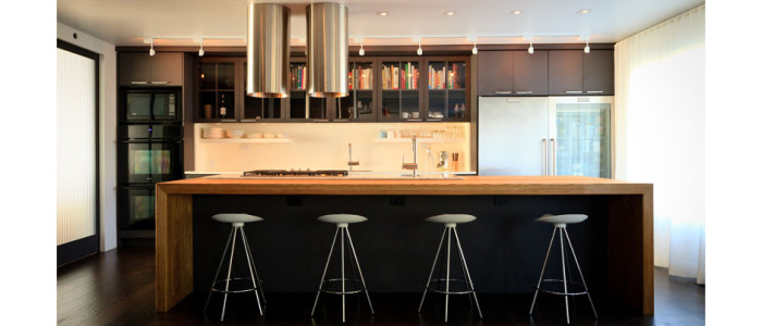 Kitchen with dark gray cabinets, a large oak island and two stainless steel tubes over the cook top, modern