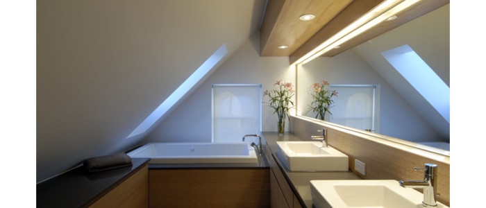 modern bathroom with vaulted ceilings, skylight over tub, and long counter with mirror and 2 white sinks