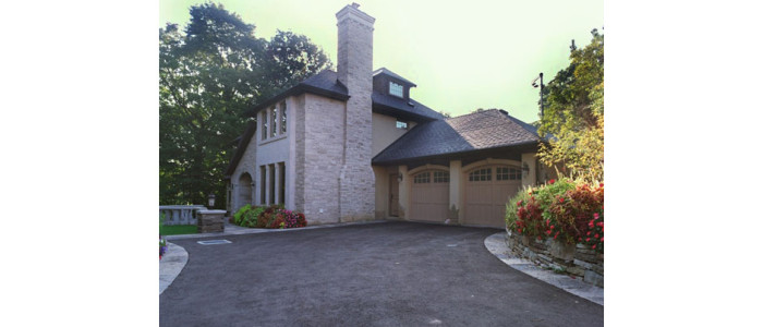 2 story gray stone home with attached tan stucco garage