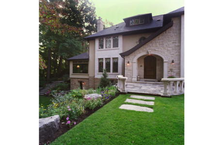 Entrance to traditional home with stone walls, stone arch over entry door and lush gardens