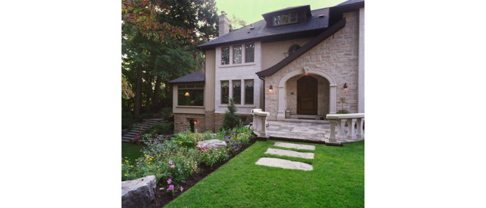 Entrance to traditional home with stone walls, stone arch over entry door and lush gardens