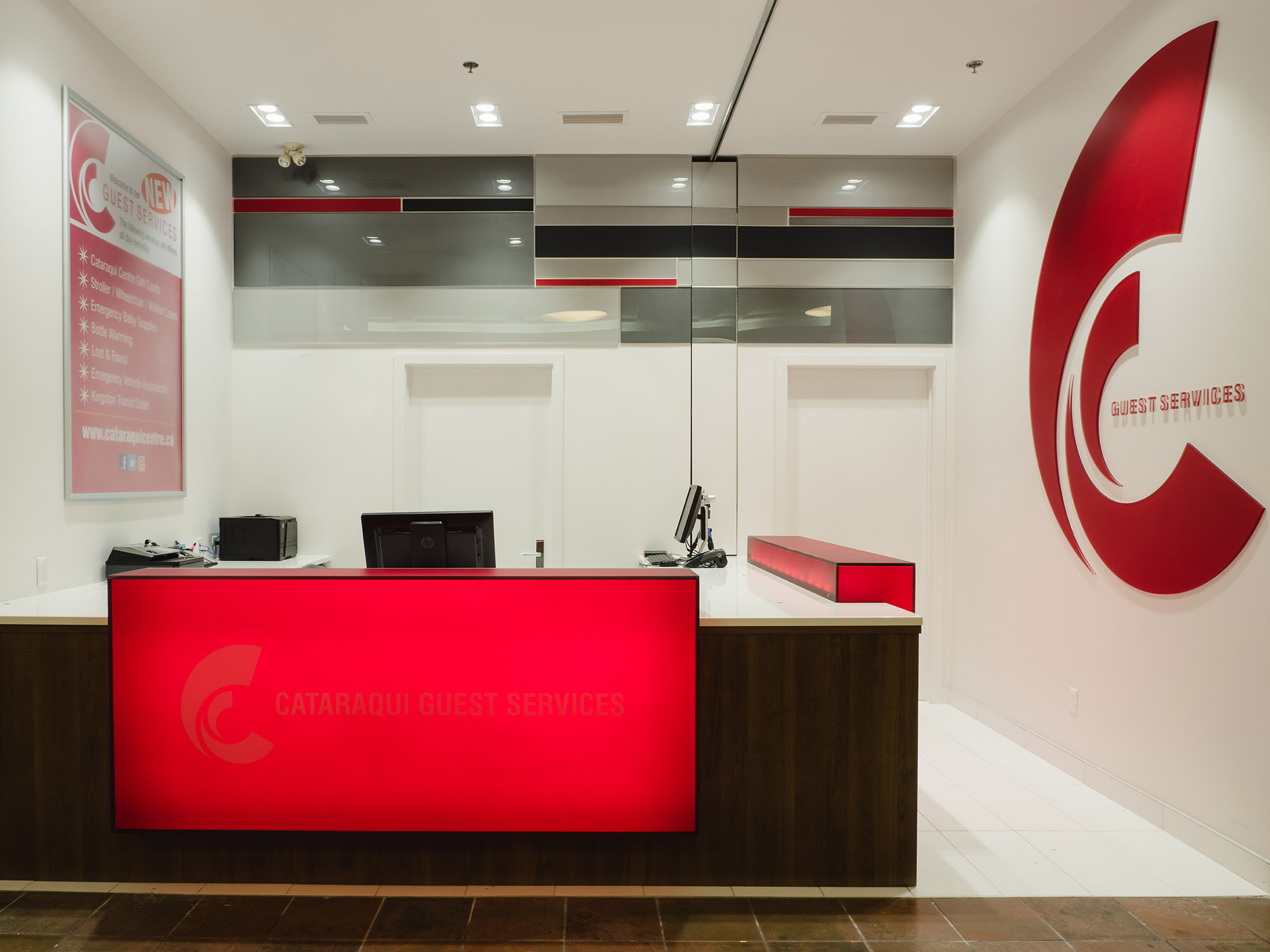Wide view of Cataraqui Centre’s guest services desk with glowing red signage and backlit service board.