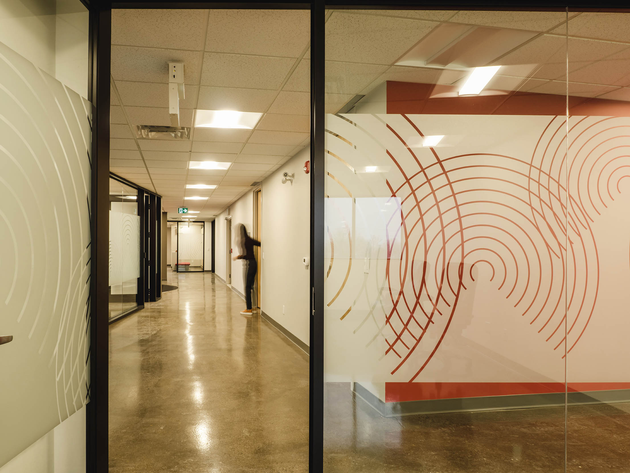 Branded glass film with concentric arcs adds privacy and identity to the corridor.