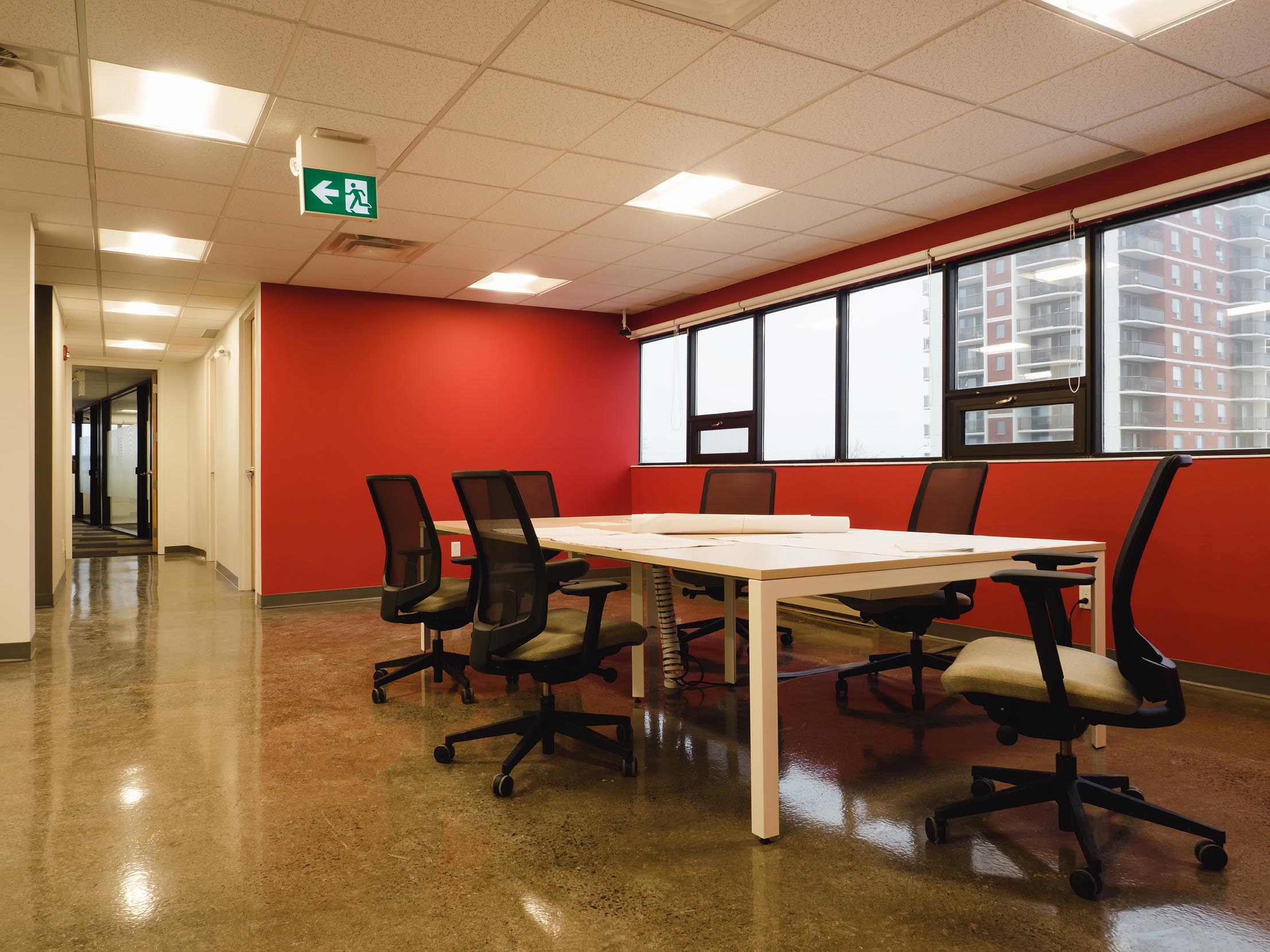 Minimalist meeting space with ergonomic chairs, white tables, and a bold red feature wall.