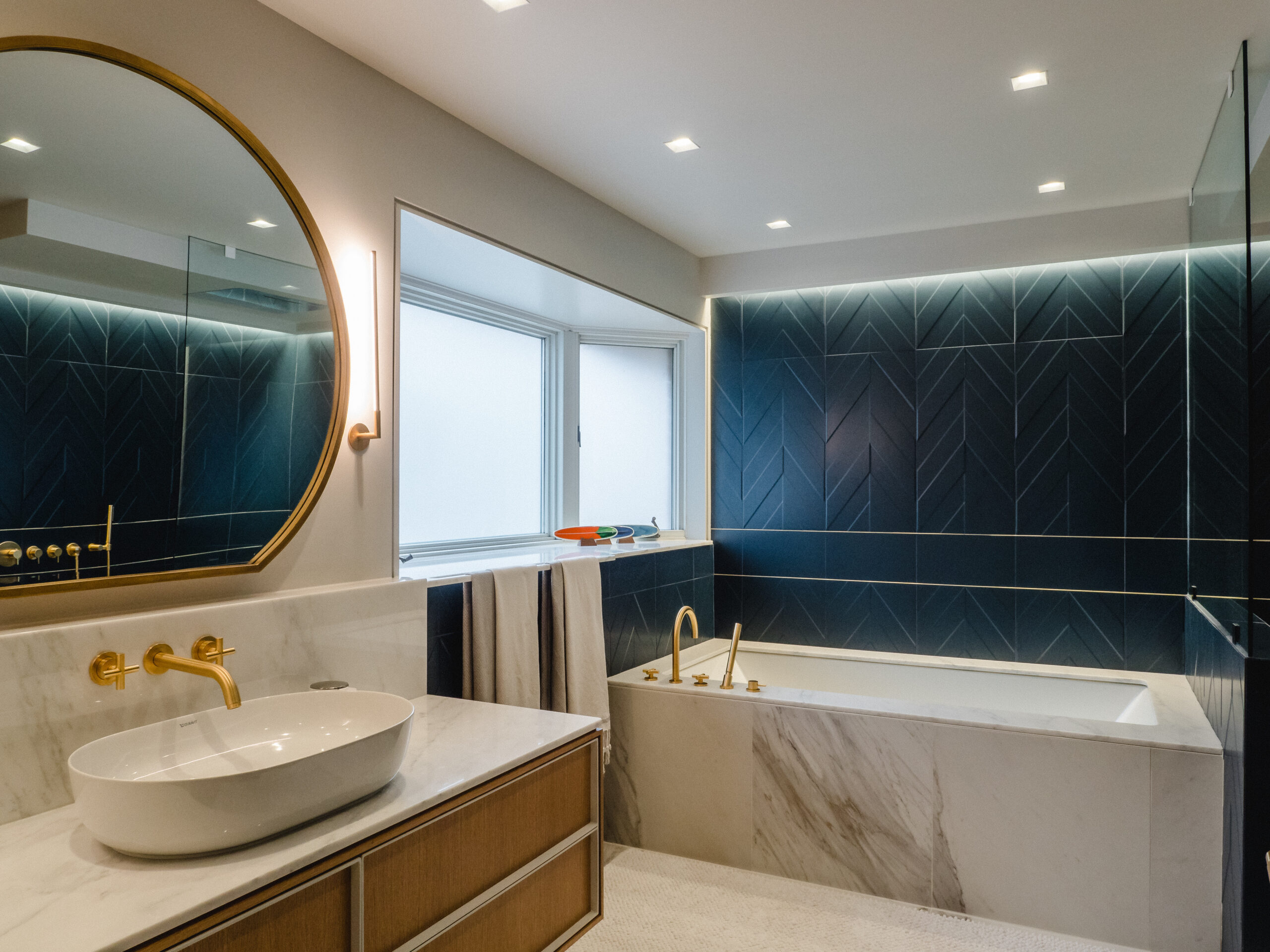 Minimalist floating vanity with round mirror and brass sconces in a contemporary ensuite with marble accents.