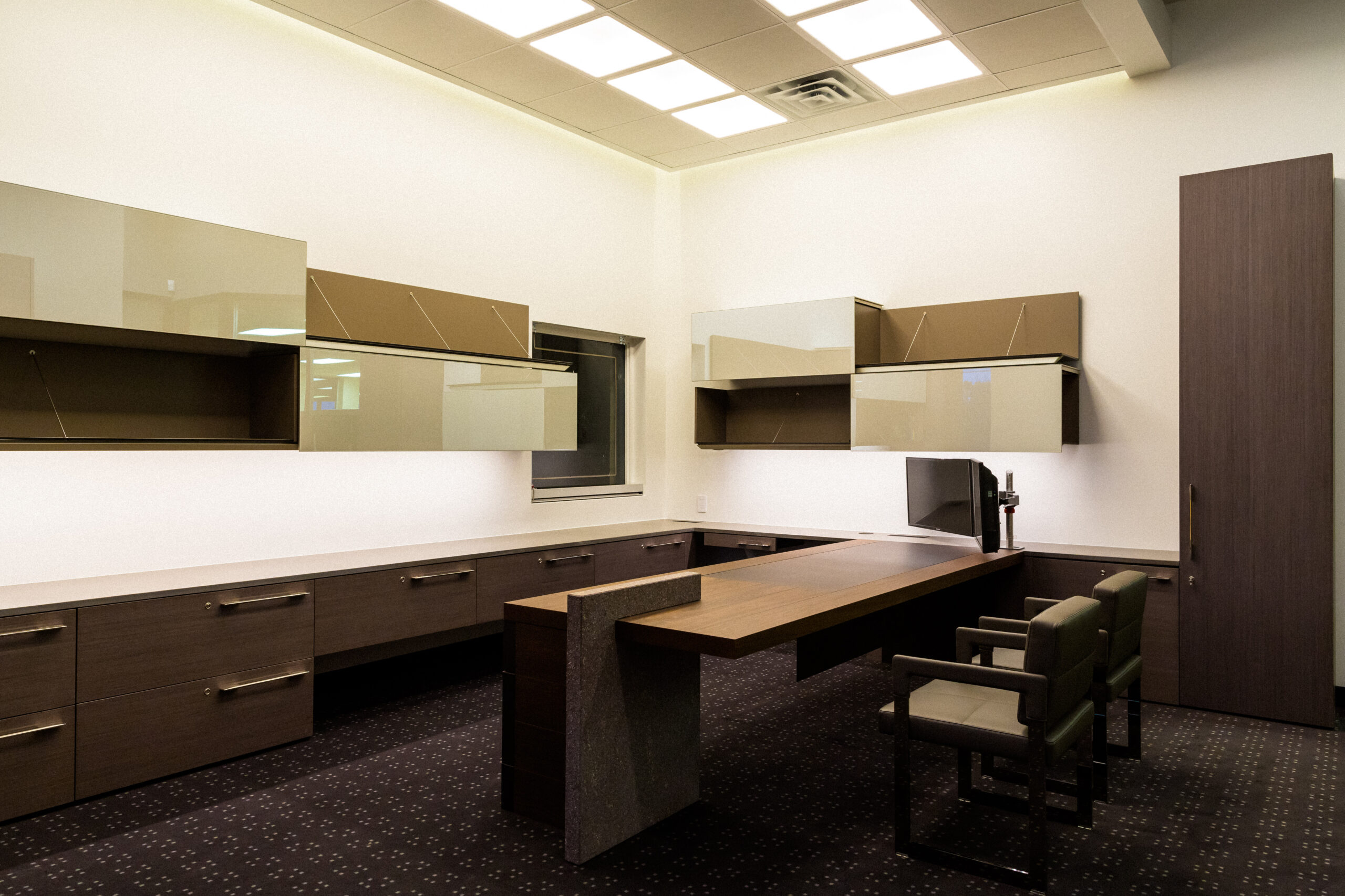Contemporary executive office featuring custom millwork, matte glass overhead cabinetry, and minimalist desk design beneath architectural ceiling lighting