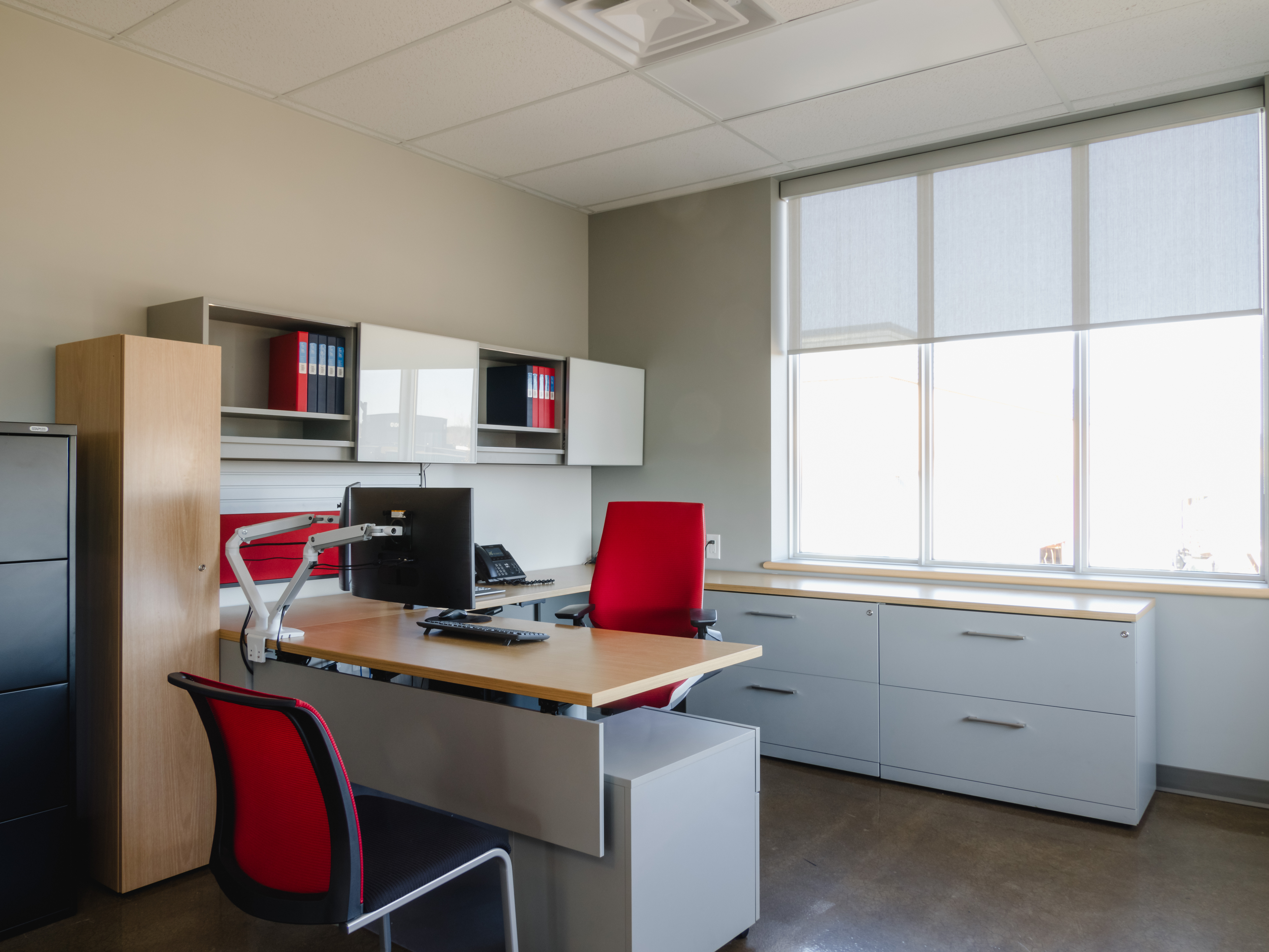 Contemporary executive office with sleek grey millwork, red accents, and expansive natural light from large windows