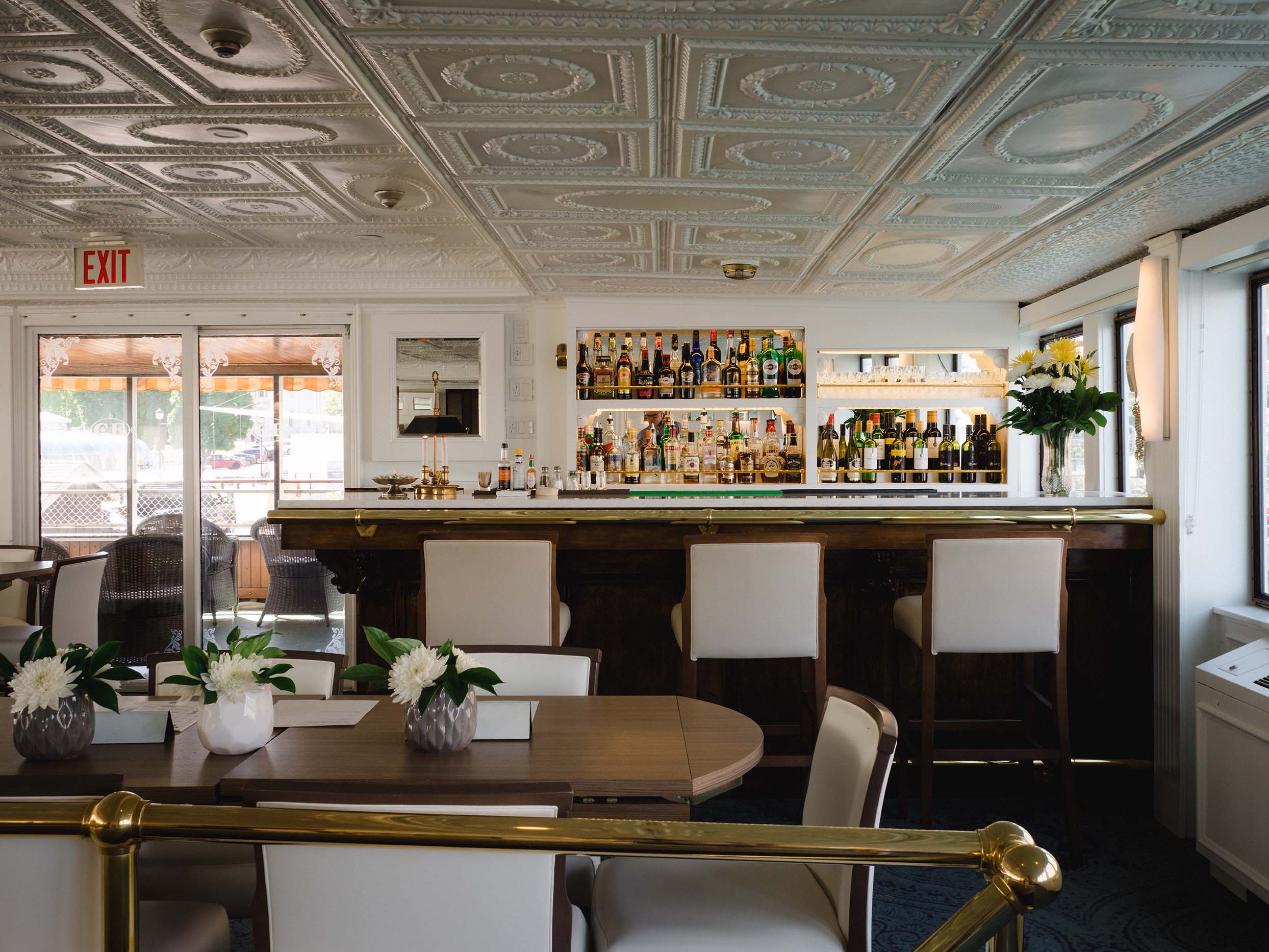 Light-filled cruise ship interior with elegant bar, white seating, and fresh floral centerpieces