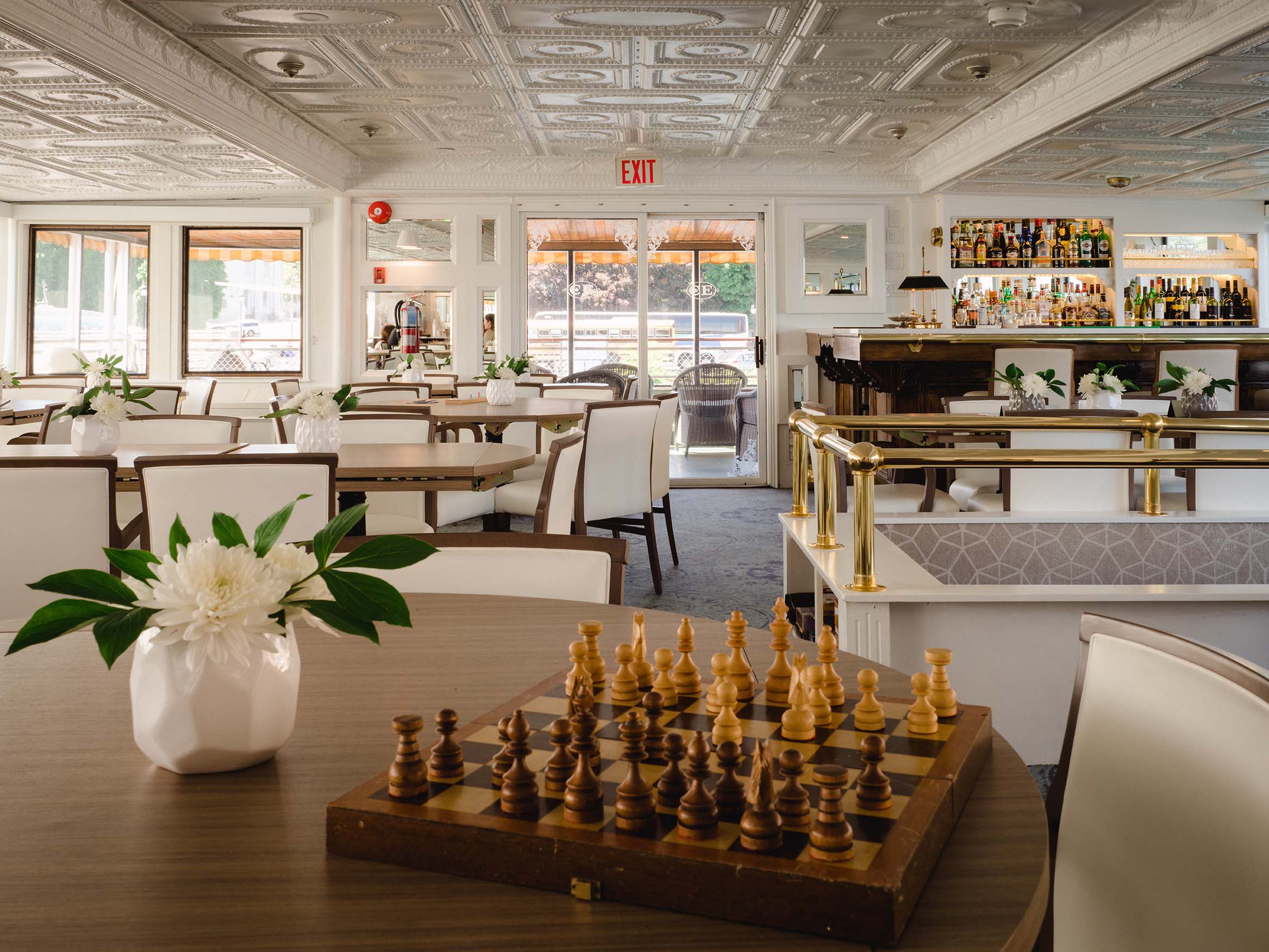 Refined ship dining lounge with white leather chairs, round tables, and vintage ceiling tiles
