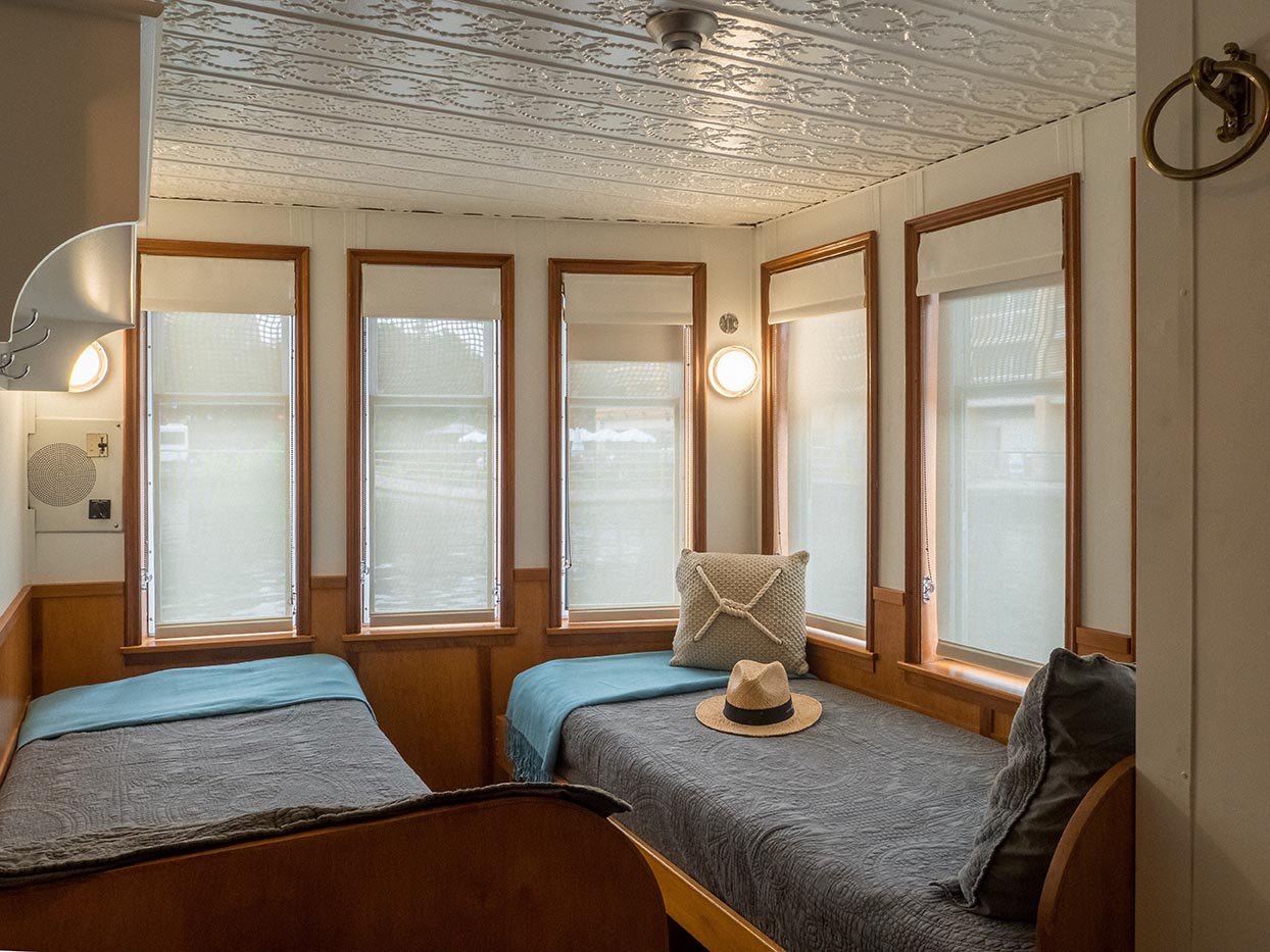 Twin cabin aboard river cruise with large windows, custom wood paneling, and built-in storage