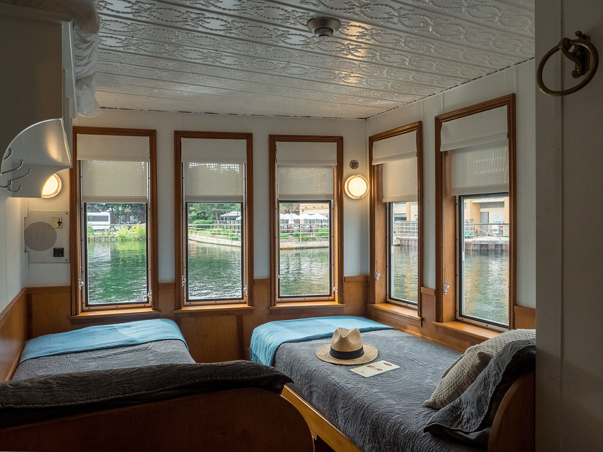 Guest room with twin beds, water views, and classic ceiling details on historic cruise ship