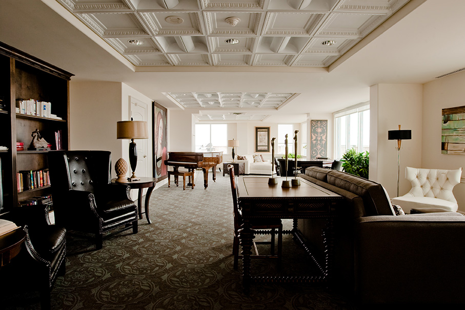 Elegant library and lounge space with tufted chairs, coffered ceiling, and grand piano