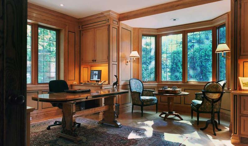 Warm wood-paneled custom home office with bay windows overlooking mature trees in a Toronto ravine lot.