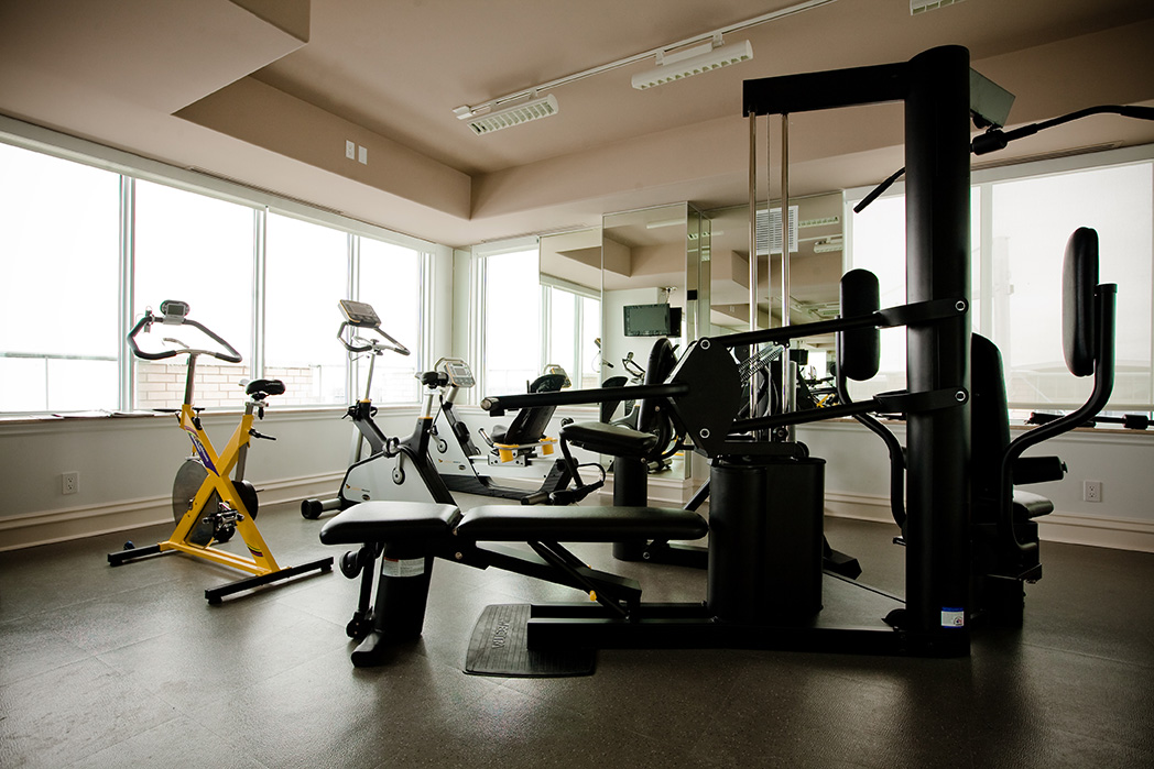 Condominium fitness room with cardio and weight equipment surrounded by windows