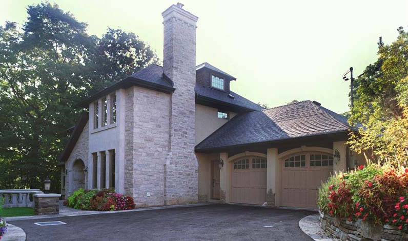 Double garage and stone facade of a Toronto ravine home, framed by vibrant garden beds and a sweeping driveway.