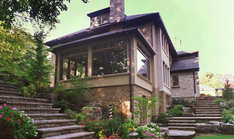 Custom home exterior with large windows, natural stone base, and garden steps leading through lush Toronto ravine landscaping