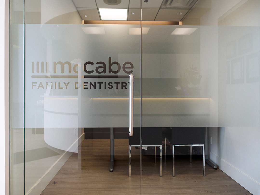 Frosted glass entry with McCabe Family Dentistry logo and warm-lit reception beyond.