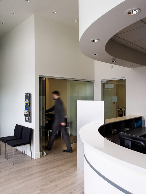 Modern curved reception desk in white with overhead lighting and wood-look flooring.