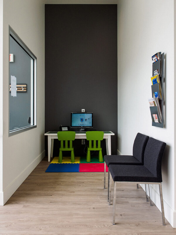 Children's play and tech corner with bright green chairs, computer station, and play mats.