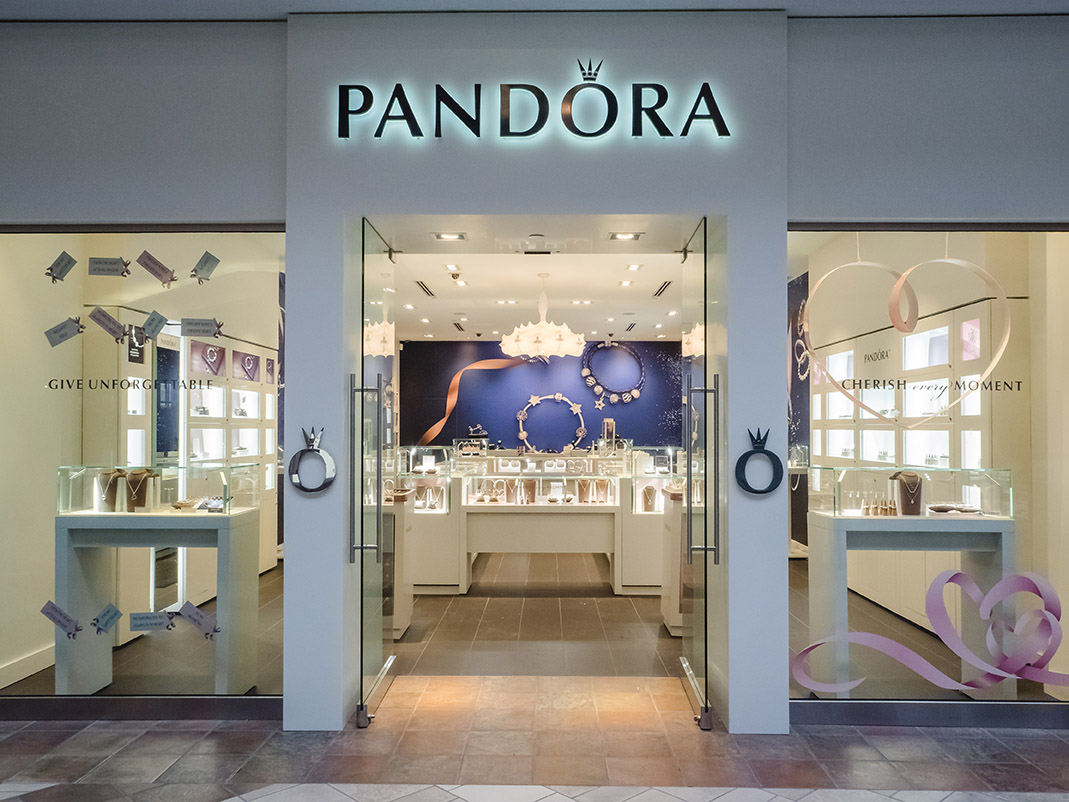 Glass storefront of the Pandora jewelry store with illuminated signage, display windows, and entry doors inside a shopping mall.