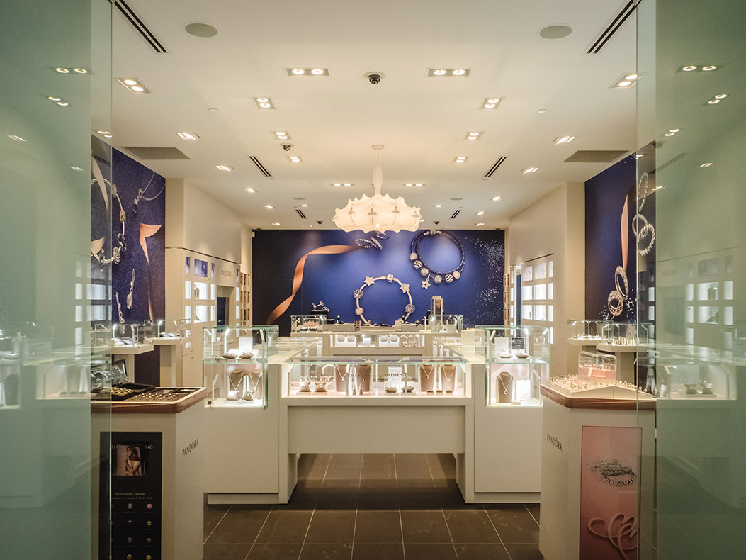 Interior view looking toward the back of the store featuring display cases, sculptural lighting, and a deep blue feature wall with jewelry graphics.