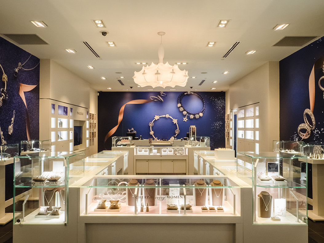 Symmetrical layout of the Pandora retail space with glass jewelry counters, central lighting, and branded wall graphics.