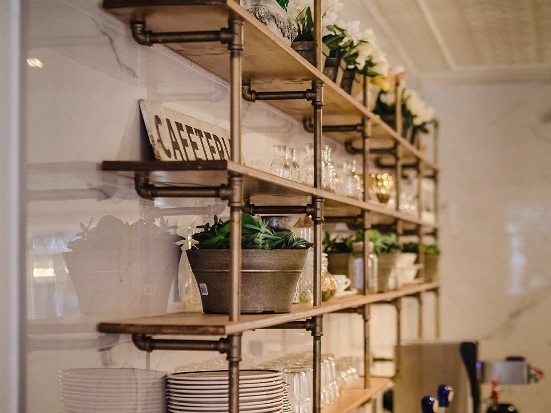 Display shelves styled with potted plants, glassware, and vintage sign reading “CAFETERIA”