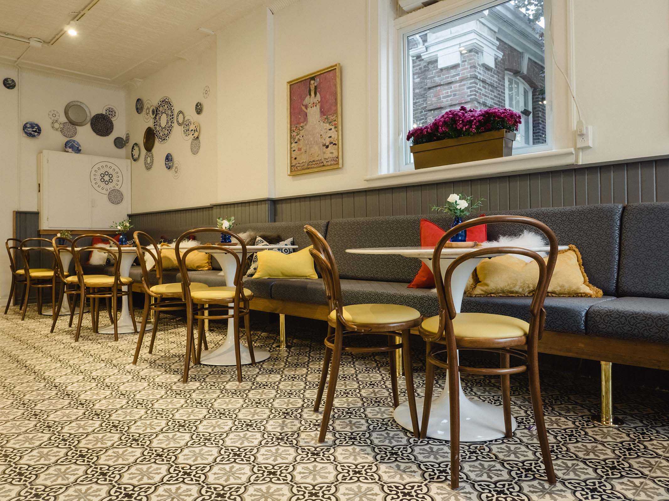 Café seating area with round tables, vintage chairs, and playful pillows against tin ceiling backdrop