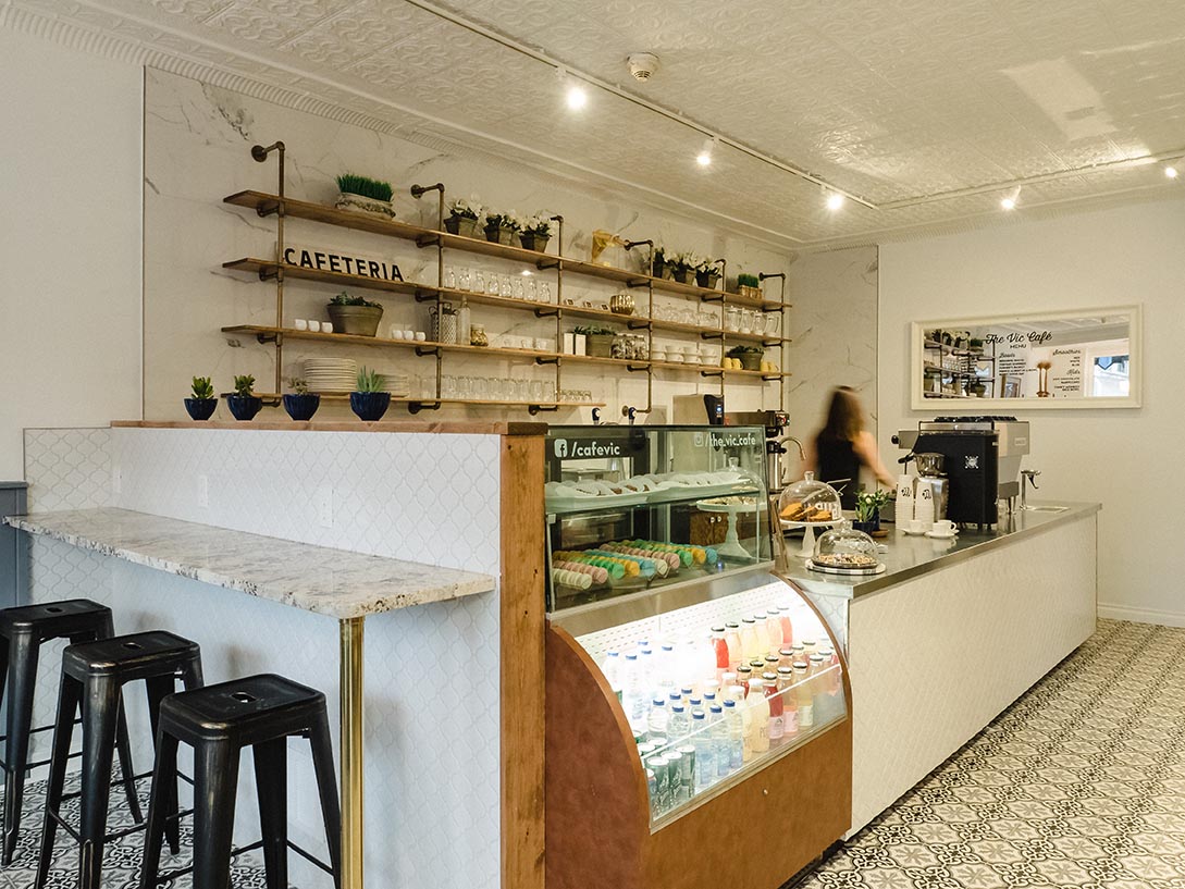 Interior shot of The Vic Café counter with open shelving, café menu board, and pastry display case.