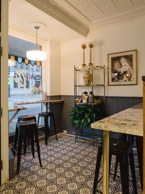 Cozy corner seating with high-top tables, black stools, and brass shelving styled with greenery and ceramics.