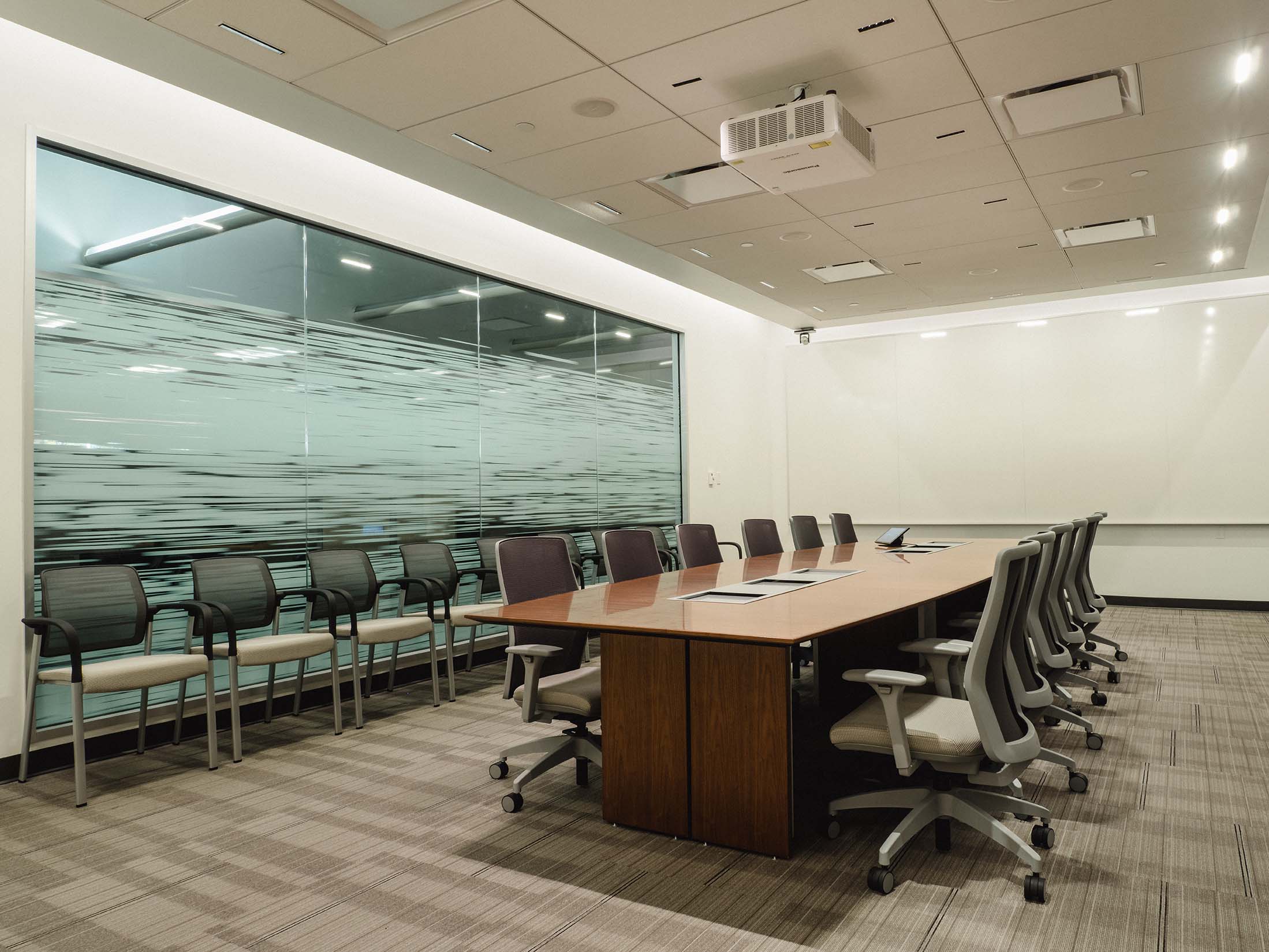 Renovated boardroom with a central wood conference table, ergonomic chairs and acoustic ceiling panels.