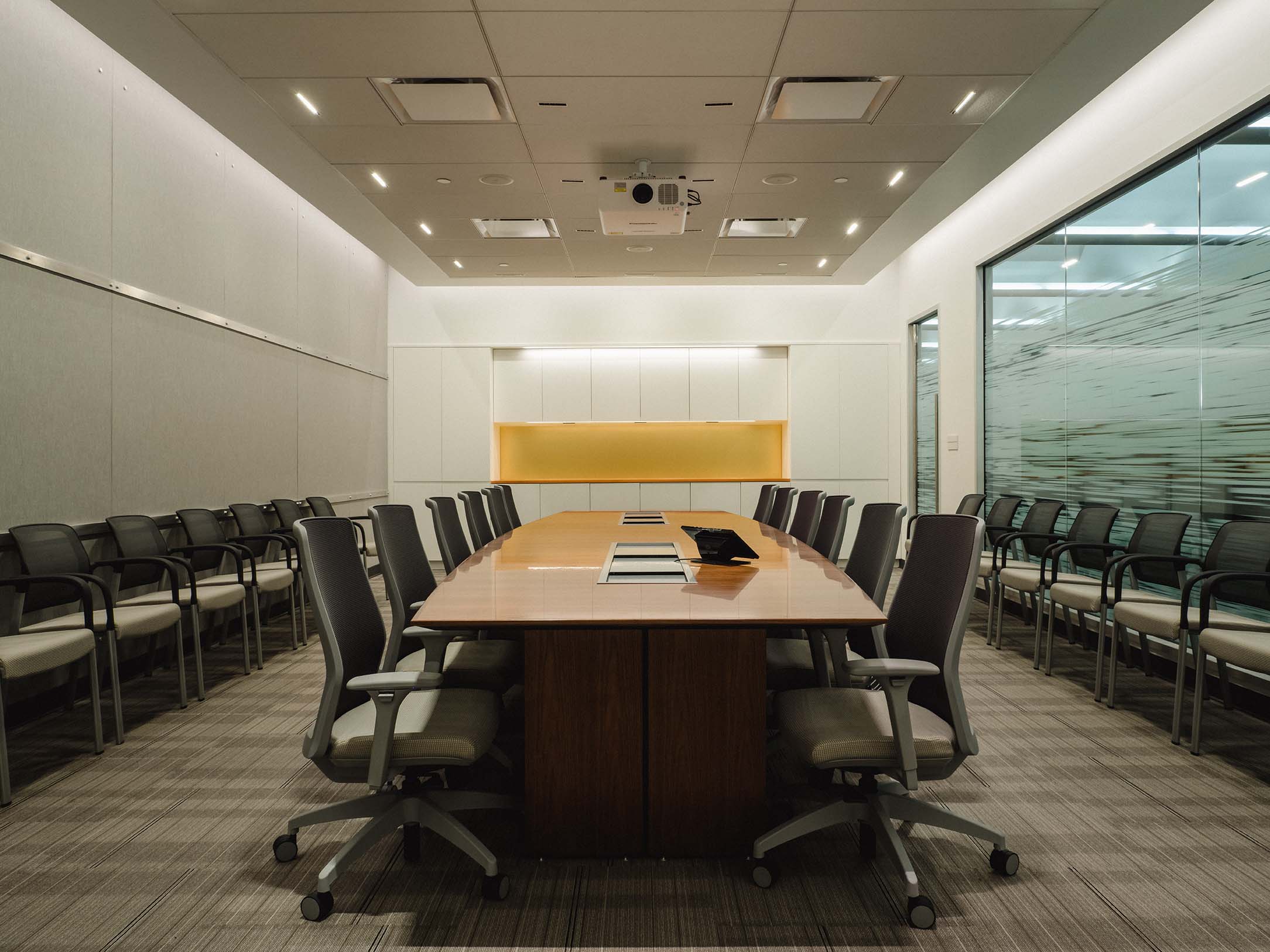 Renovated boardroom with a central wood conference table, ergonomic chairs, acoustic ceiling panels, and modern lighting.