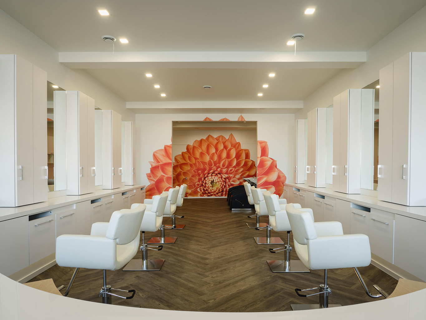 Bright, modern salon interior with white styling stations and a vivid orange dahlia mural.