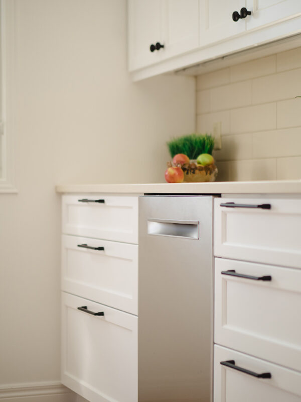Side view of integrated dishwasher within a bank of white cabinetry and classic subway tile backsplash.