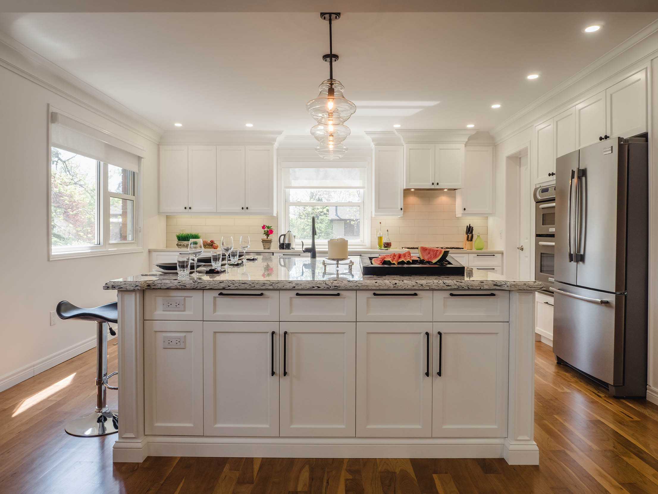 Wide-angle view of the full kitchen featuring white shaker cabinetry, a large island, pendant lighting, and stainless steel appliances.