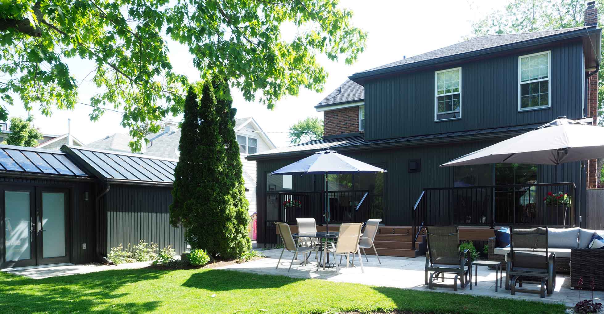 View of rear yard showing black addition, modern deck, and landscaped patio