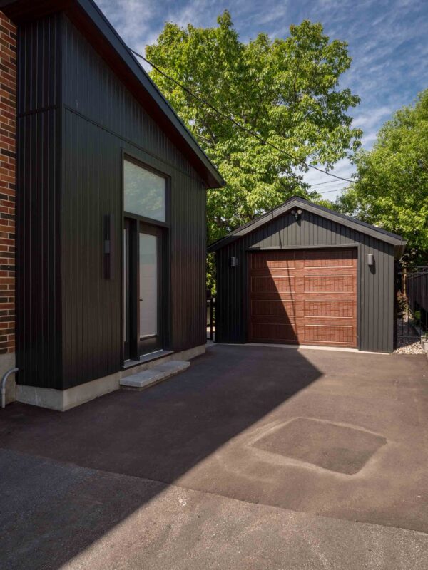 Black vertical siding and matching detached garage with wood-look door