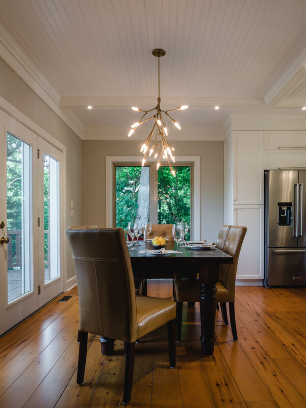 A dark wood table surrounded by leather chairs under a brass chandelier with exposed bulbs.
