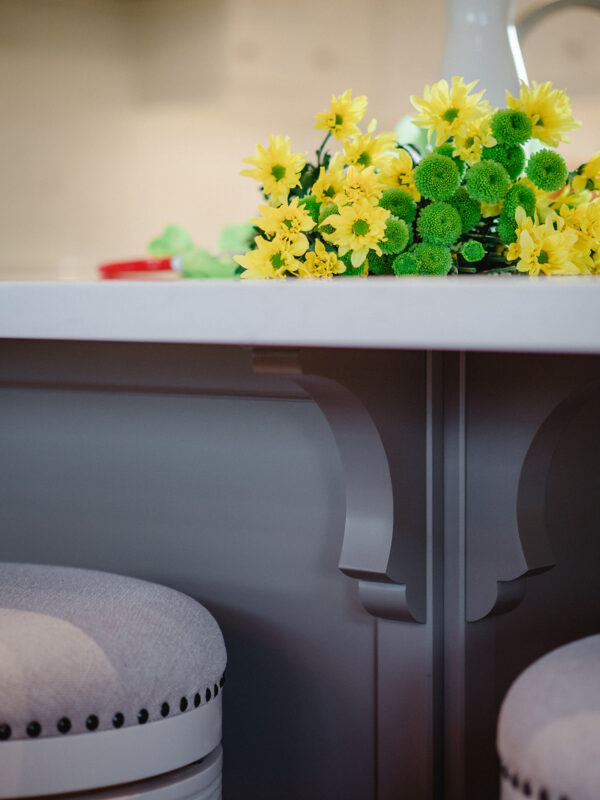 Close-up of white bar stools and decorative island brackets, with yellow flowers adding a pop of colour.