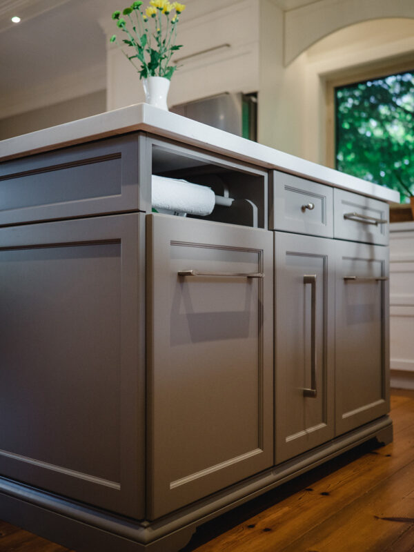 A detail of a grey island with custom millwork, white quartz countertop, and integrated paper towel holder.