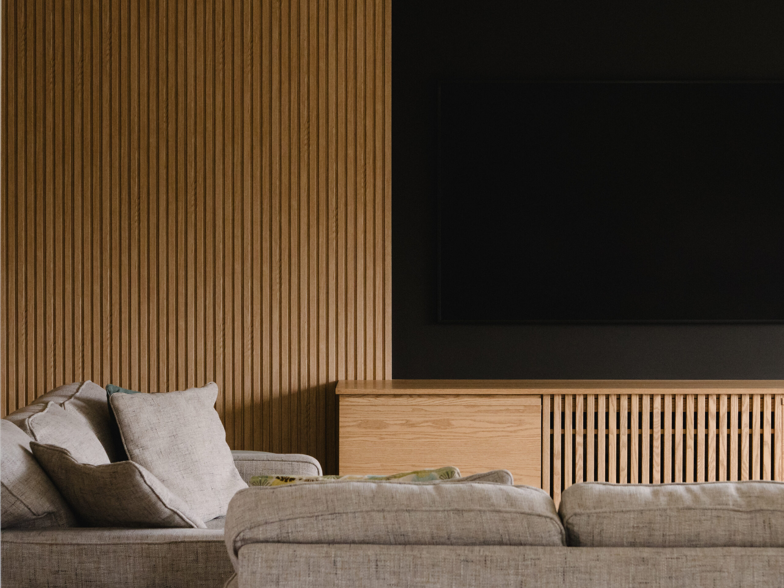 Modern living room with black feature wall, slatted oak media wall, and floating wood console